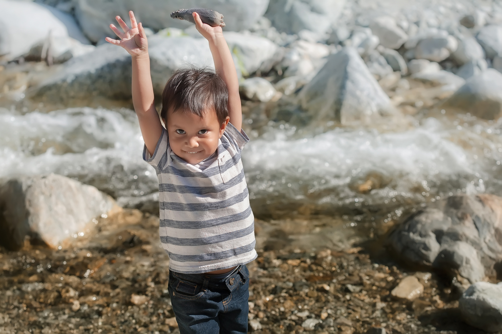 A latino boy expressing happiness and joy, standing near the shore of a river during summer camp.