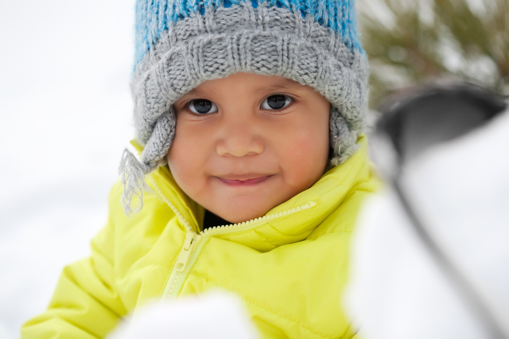 Cute Latino toddler smiling while playing in the snow during winter and wearing a knit hat.